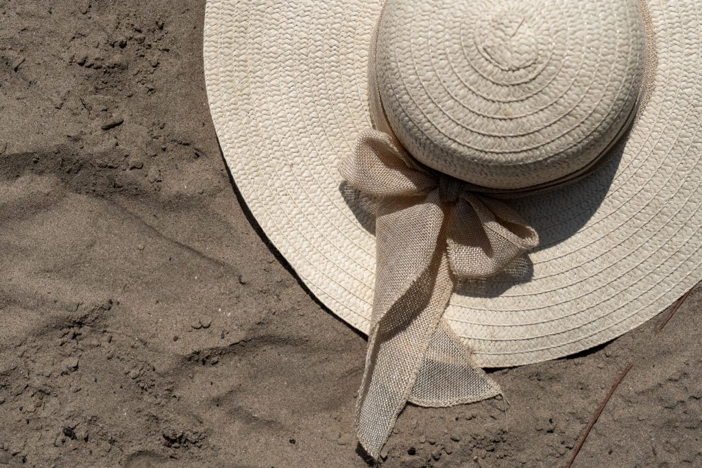 Links oben ist ein Strohhut zu sehen. Der Untergrund ist brauner Sand.